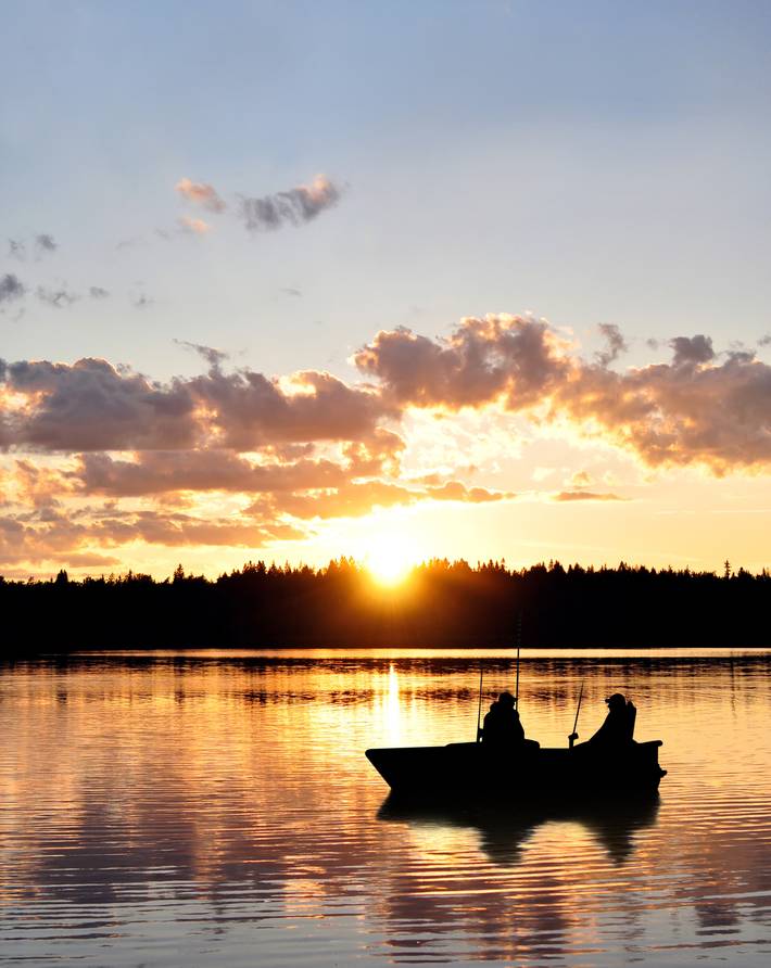 zeigt zwei Angler bei Sonnenuntergang auf kleinem Boot
