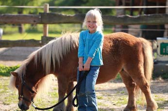 Kleines Mädchen steht lächelnd bei einem Pony